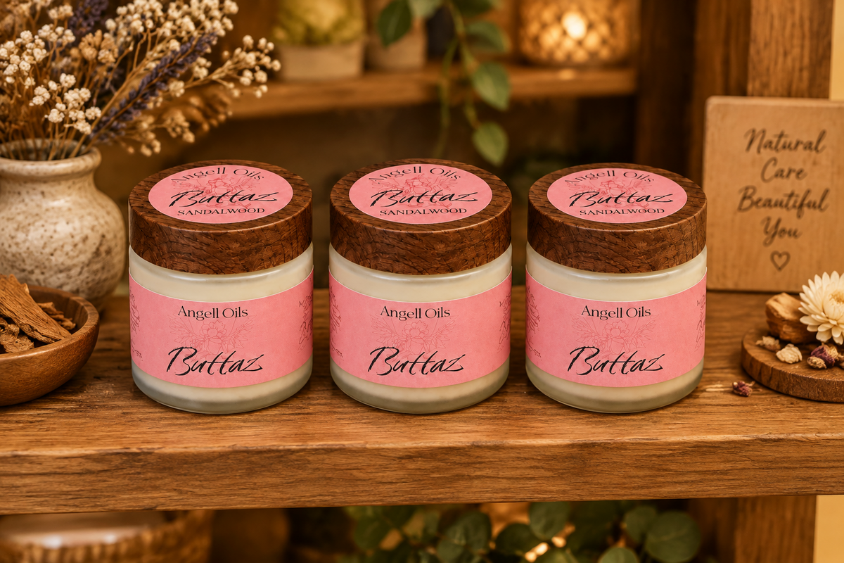 A small glass jar candle with a pink label reading 'Angell Oils Buttz SANDALWOOD' and a round dark wood lid, photographed on a clean white background.